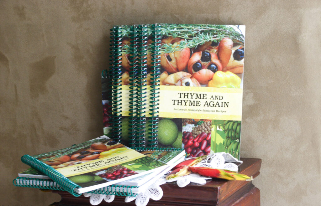 Copies of the cookbook Thyme and Thyme Again, authentic Jamaican recipes, stacked on a table